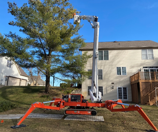 An arborist pruning a tree on a spider crane on a residence in Michiana.